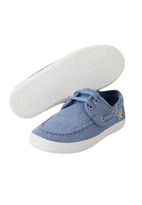 Zapato de lona azul con suela de goma blanca, puntera redonda y costuras ligeras. Presenta cordones y un acento de logo amarillo en el costado.