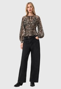 Μπλούζα με λουλουδάτο σχέδιο, ελαστική μέση και μακριά μανίκια, συνδυασμένη με μαύρο τζιν παντελόνι με φαρδιά πόδια και ψηλοτάκουνες μαύρες μπότες μέχρι τον αστράγαλο.