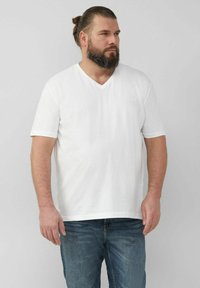 Weißes Baumwoll-T-Shirt mit kurzen Ärmeln und V-Ausschnitt, entspannter Schnitt, zeichnet sich durch ein schlichtes Design ohne Muster oder Akzente aus, getragen mit blauen Jeans.