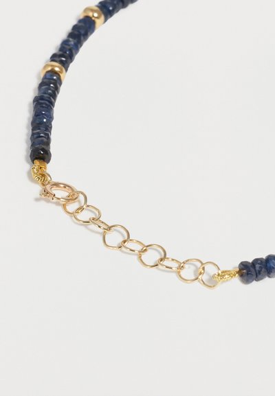 Κοντινή λήψη μπλε κολιέ με χάντρες και χρυσά διαχωριστικά χάντρες καθώς και χρυσή επέκταση αλυσίδας με κούμπωμα σε σχήμα αστακού σε λευκό φόντο.