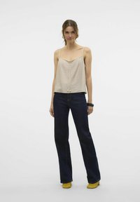 Beige geplooide camisole top met dunne bandjes, gecombineerd met donkerblauwe flared jeans en gele hakken. Eenvoudig ontwerp, zachte textuur.