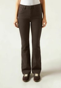 Jean évasé marron avec une texture lisse, un design �à cinq poches et une fermeture éclair. Associé à des baskets en daim marron avec des lacets crème.