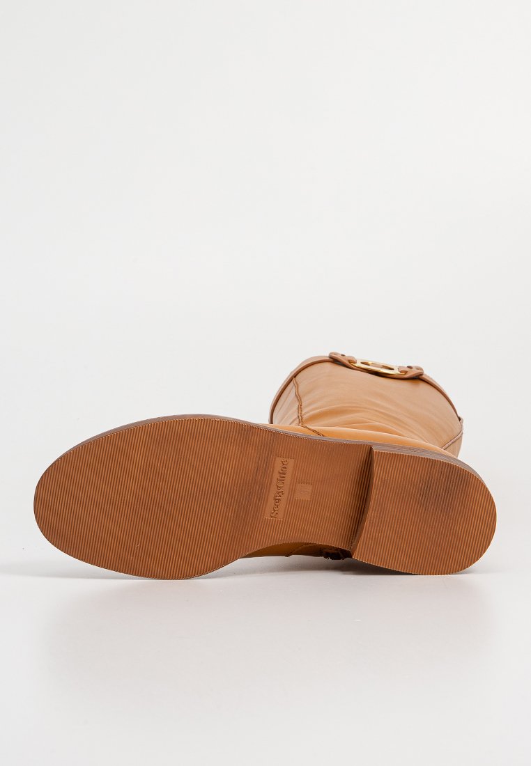 Tanskleurige waterdichte laars met een glad bovenwerk, platte rubberen zool en een ronde gouden accent aan de zijkant. Geavanceerde zool voor grip en stabiliteit.