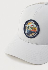 Ανοιχτό γκρι καπέλο με στρογγυλεμένη γείσο. Διαθέτει κυκλικό κεντητό σχέδιο με πολύχρωμα βουνά και ήλιο. Ρυθμιζόμενο λουράκι στο πίσω μέρος.