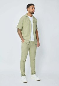 Chemise vert clair à manches courtes en tissu texturé, assortie à un pantalon de jogging. Portée avec un t-shirt blanc et des baskets blanches.