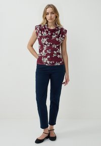 Top in tessuto floreale bordeaux con scollatura a cowl e maniche corte, con lati arricciati; abbinato a pantaloni blu navy aderenti. Ballerine nere con cinturino alla caviglia completano l'outfit.