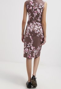 Brun blomsterkjole med lyserøde og hvide blomster, tætsiddende design, knælængde, satinmateriale og en slids bagpå for nem bevægelse.