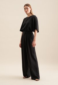 Czarna, luźna koszulka i spodnie o szerokich nogawkach wykonane z lekkiego materiału, z prostym wzorem, okrągłym dekoltem i plisami w spodniach.