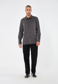 Dark gray button-up shirt with a subtle ribbed texture, paired with black trousers and black athletic shoes, on a plain background.