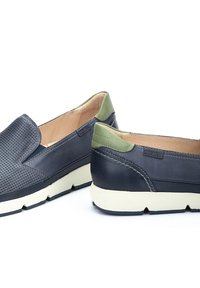 Zapatos de cuero azul marino de tipo slip-on con parte frontal perforada, acento verde en el talón y suela de goma crema con acabado texturizado.