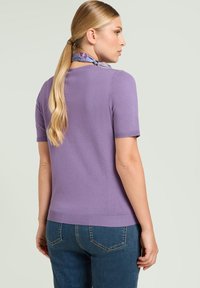 Suéter de punto de manga corta en color lavanda con dobladillo acanalado, combinado con jeans azules. Presenta una textura suave y vista trasera, mostrando el cabello recogido.