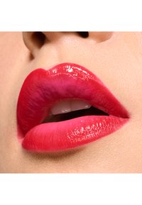 Close-up van glanzende rode lippen, met een verloop van diep rood naar roze, een gedefinieerde vorm en een gladde textuur tegen een lichte huid.