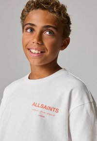 Bílý bavlněný tričko s krátkým rukávem, na levé straně s oranžovým logem "ALLSAINTS" a japonským textem. Hladká textura.