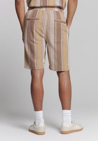 Gestreepte shorts in aardetinten van bruin, beige en geel. Heeft een relaxte pasvorm, twee achterzakken en een geribbelde textuur. Draagt met sneakers en sokken.
