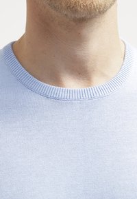 Pulover tricotat de culoare albastru deschis, având un guler rotund ribatat, o textură netedă și un model de cusătură uniform, concentrându-se pe zona superioară a pieptului.