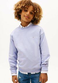 Lys lavendel sweatshirt med ribbede manchetter og halsudskæring. Har et lille logo på brystet. Bæres over en skjorte med krave og denimjeans.