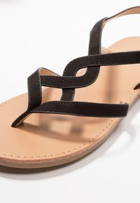 Mustat nahkaiset sidosandalsit, joissa on kudotut hihnat ja vaaleanruskea synteettinen pohja. Varustettu kevyellä pehmustuksella ja tikatuilla koristeilla reunoilla.