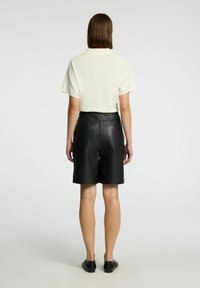 Shorts en cuir noir taille haute avec plusieurs poches, associés à un haut crème ample, vus de dos.