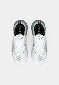 Chaussures de sport blanches avec détails en mesh, semelle grise translucide et accents noirs. Elles comportent des lacets et un logo sur la languette.