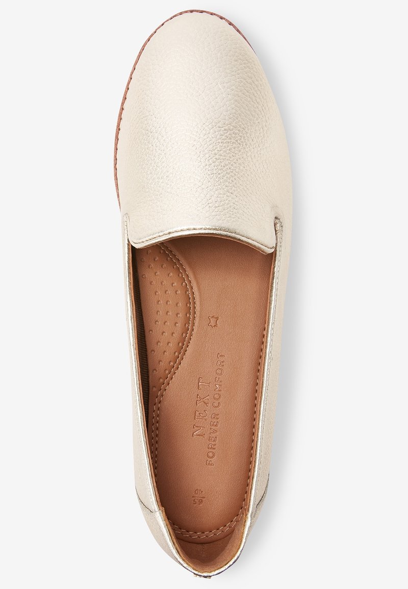 Chaussure sans lacets de couleur crème avec une tige texturée, un bout rond et une semelle intérieure en cuir lisse. Détail notable : logo de la marque embossé à l'intérieur.