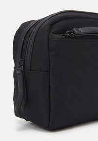 Trousse de maquillage en nylon noir de forme rectangulaire, avec une fermeture éclair, une texture douce et une petite poignée latérale pour un transport facile.