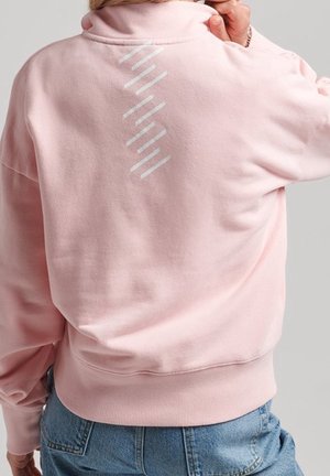 Różowy krótki sweatshirt z wysokim kołnierzem i prążkowanymi mankietami, z ząbkowanym wzorem teksturowanym w odblaskowym wykończeniu na plecach.