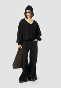 Black cropped sweatshirt with a V-neck, paired with high-waisted black flared jeans. Accessories include a knit beanie and dark sunglasses.