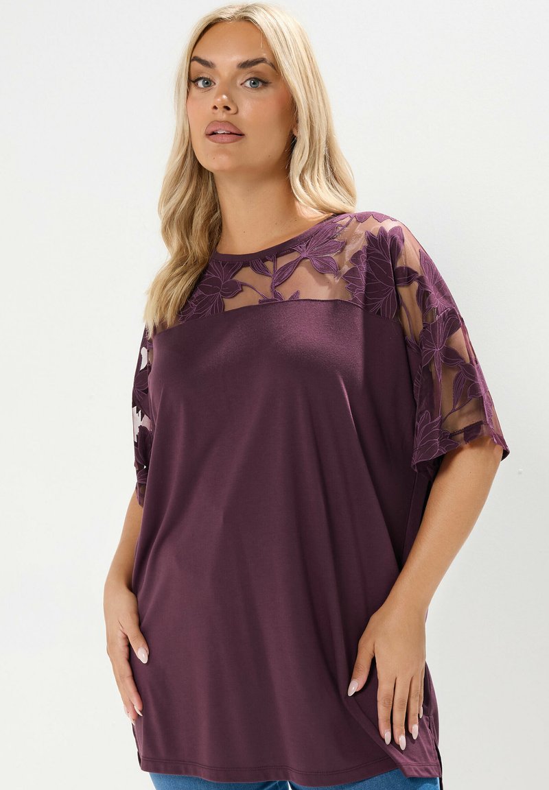Lila tunika med genomskinliga ärmar med blommönster, rund halsringning och avslappnad passform. Tillverkad av mjukt, lätt tyg.
