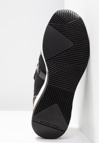 Semelle de basket noire en caoutchouc texturé pour une meilleure adhérence, avec une semelle intermédiaire blanche et un logo. Avant-pied arrondi, design minimaliste, avec un motif de bande de roulement géométrique.