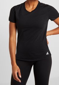 Maglietta sportiva nera a maniche corte realizzata in tessuto morbido con scollatura a V. Presenta un piccolo logo Adidas bianco sul lato sinistro inferiore.