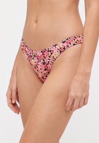 Cvetni bikini spodnji del z črno podlago in roza ter smetanastimi cvetovi. Izdelan iz gladkega materiala, z nizkim rezom in minimalno pokritostjo.