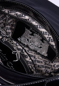 Interno di una borsa nera con una fodera a motivo che presenta il nome del marchio. Include accenti in argento, una tasca con zip e dettagli in catena.