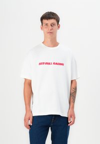 Hvit bomull t-skjorte med korte ermer, med en rød "RED BULL RACING" grafikk over brystet. Brukt sammen med blå jeans.