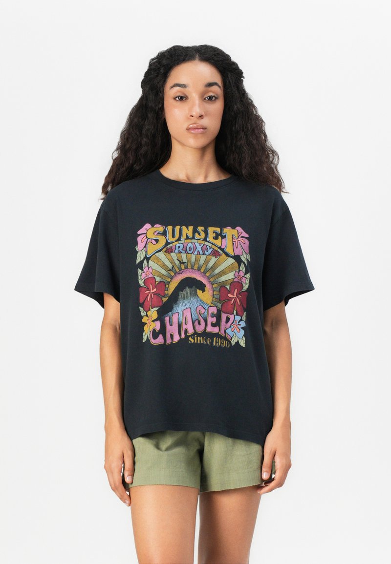 T-shirt en coton noir avec un graphique coloré sur le devant représentant des fleurs tropicales, des vagues et des rayons de soleil. Coupe ample et manches courtes.