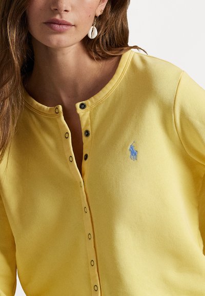 Yellow button-up top featuring a textured fabric, short sleeves, and a small blue embroidered logo on the left chest area.