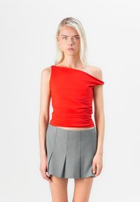 Top rojo de un solo hombro con textura fruncida, combinado con una minifalda plisada gris. Enfócate en la suavidad de la tela y en los colores contrastantes.