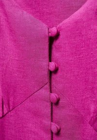 Robe en lin fuchsia avec un col en V et des boutons ronds décoratifs sur le devant, présentant une texture subtile et des éléments de design géométriques.