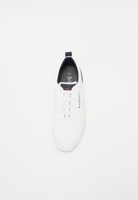 Fehér sneaker perforált textúrával, rugalmas fűzőkkel és sötétkék díszítéssel a saroknál. A talpbetéten 42-es méret van feltüntetve.