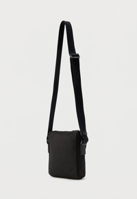 Μαύρη τσάντα ώμου με ορθογώνιο σχήμα, με εξωτερικό υφασμάτινο υφή, ρυθμιζόμενο ιμάντα και κλείσιμο με φερμουάρ στο πάνω μέρος.