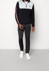 Svart fleece-tröja med ljusgrå överdel, dragkedja vid halsen och färgglada sidostripes. Matchad med svarta cargobyxor och vita sneakers.