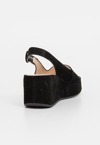 Des sandales à talons compensés en suédine noire présentent un bout ouvert arrondi, une bride arrière avec élastique et une plateforme texturée pour plus de hauteur.