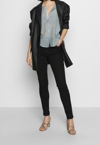 Musta nahkatrenssi, vaaleansininen nappipaita, mustat tiukat farkut ja eläinkuosilla varustetut avokkaat. Raskaskudoksinen kangas ja muotoon ommeltu istuvuus.