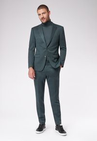 Turkusowy garnitur z dopasowaną marynarką i pasującymi spodniami, w zestawieniu z ciemnym golfem i czarnymi trampkami. Gładka faktura, klasyczny design.