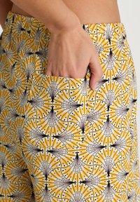 Katoenen broek met een geel en wit patroon van waaiervormen omrand met zwart, voorzien van een zijzak voor gemak.