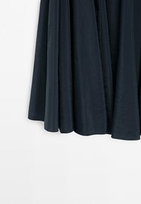 Mørk marineblå nederdel i flydende stof med bløde folder, hængende mod en ensartet hvid baggrund.