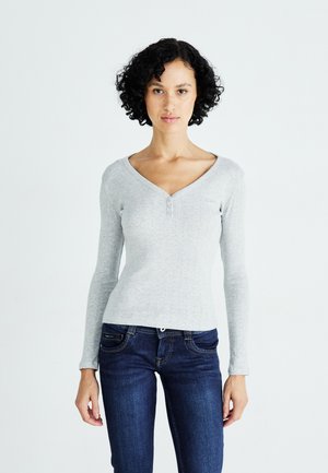 Maglietta grigia chiara a maniche lunghe con scollatura a V e chiusura con bottoni. Tessuto a costine e design aderente abbinato a jeans di jeans scuri.