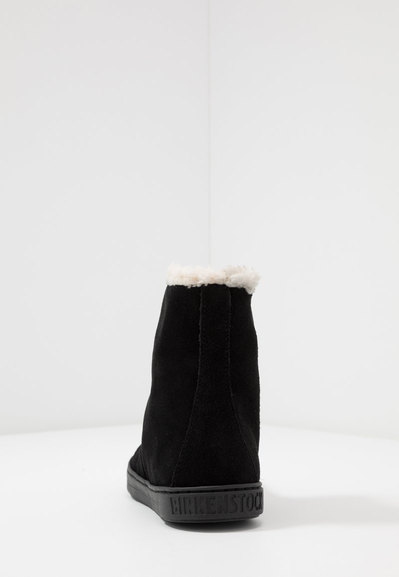 Schwarze Wildleder-Stiefeletten mit einer strukturierten Oberfläche und einem weichen weißen Fellbesatz oben. Gummisohle mit „BIRKENSTOCK“-Markierung an der Seite.