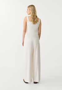 Ljus linne jumpsuit i off-white, med fyrkantig halsringning, vida ben och elastisk midja. Slät textur med minimal detaljering.