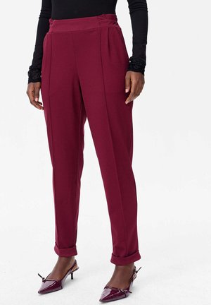 Pantalons taillés bordeaux avec plis et taille haute, présentant une texture lisse et des ourlets roulés, associés à des chaussures pointues bordeaux.