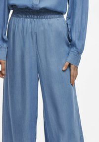 Pantaloni in denim azzurro chiaro a gamba larga con vita elastica, texture morbida e tasche laterali, dal taglio rilassato.